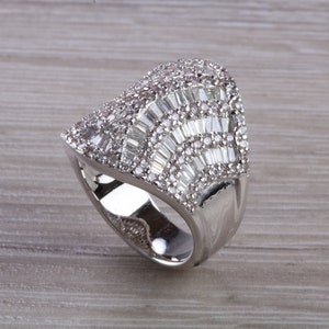 May include: A silver ring with a large, faceted, clear stone set in a geometric design.