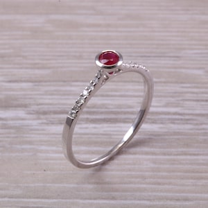 May include: A delicate silver ring with a single red gemstone and a row of small clear gemstones.