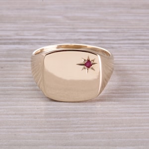Puede incluir: Un anillo de sello de oro con una piedra preciosa roja engastada en forma de estrella.