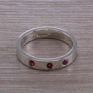 May include: A silver band ring with three small red gemstones set into the band.