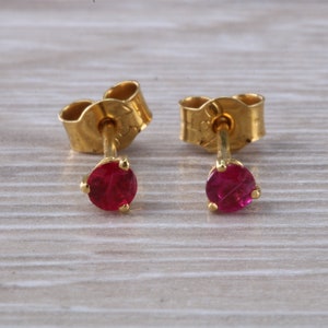 Puede incluir: Un par de pendientes de oro con pequeñas piedras de rubí redondas de color rojo.