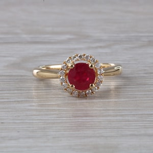 May include: A gold ring with a red ruby gemstone surrounded by a halo of smaller diamonds.