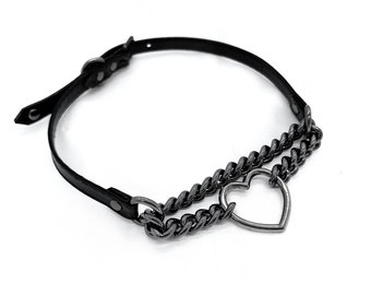May include: Black leather choker necklace with a gunmetal chain and a heart-shaped pendant. The necklace has an adjustable buckle closure. The chain is layered below the leather band.