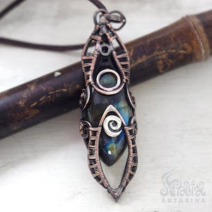 May include: A silver and copper wire wrapped pendant featuring a dark blue labradorite gemstone. The pendant is shaped like a teardrop and has an intricate wire design.