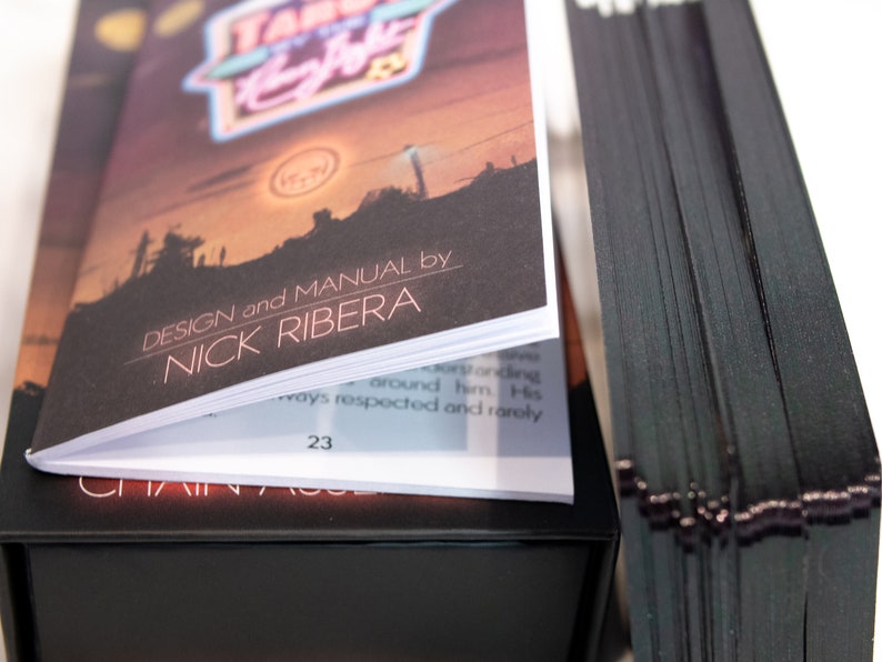 Puede incluir: Una baraja de tarot con cartas de bordes negros y un manual de instrucciones. La portada del manual muestra una ilustraci&oacute;n de un paisaje al atardecer, el texto "TAROT BY THE Neon Light" y "DESIGN and MANUAL by NICK RIBERA" con la p&aacute;gina 23.