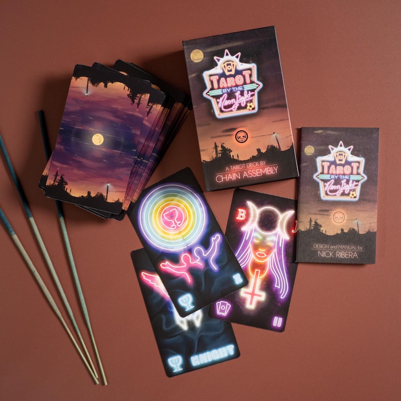 Puede incluir: Una baraja de tarot Tarot by the Neon Light que incluye una caja con un paisaje de atardecer y texto estilo ne&oacute;n. Se muestran varias cartas con ilustraciones de ne&oacute;n vibrantes de figuras, s&iacute;mbolos y copas sobre fondos oscuros, junto a tres varitas de incienso.