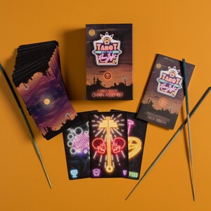 Puede incluir: Una baraja de tarot Tarot by the Neon Light que incluye una caja con texto estilo ne&oacute;n, un mazo de cartas con un paisaje a la luz de la luna y cartas individuales con ilustraciones de ne&oacute;n de calaveras, cerebros y s&iacute;mbolos, con dos inciensos.