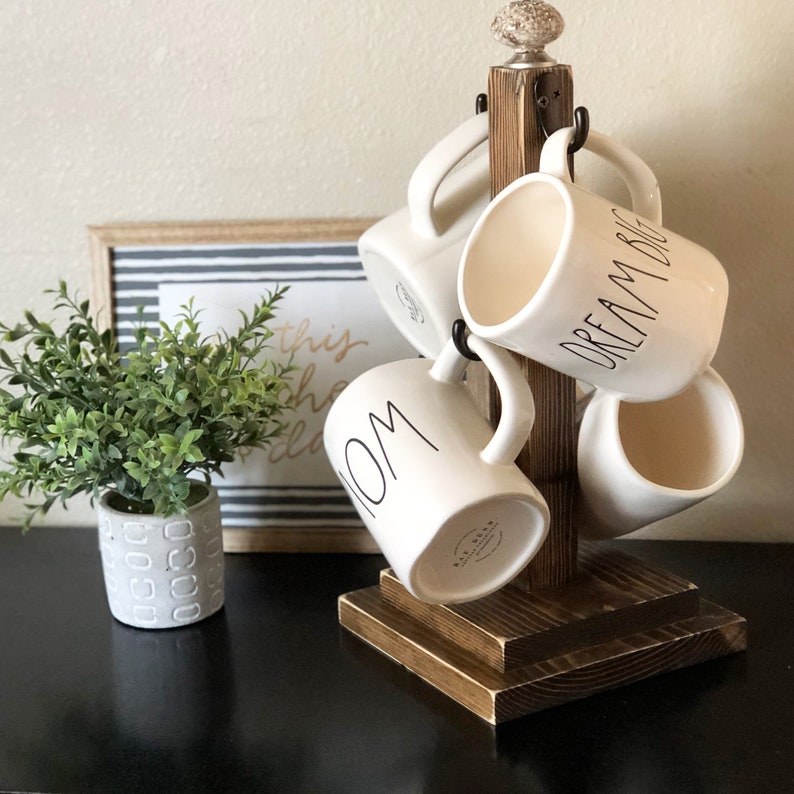 May include: Wooden mug rack with four white ceramic mugs. The mugs have black lettering that reads "Mom", "Dream Big", and "This is the place".