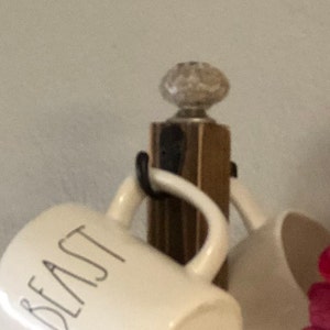 May include: A wooden mug rack with a white ceramic knob on top. The rack is holding two white mugs, one with the word "Beast" printed on it.