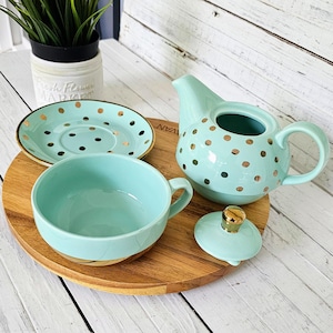 May include: A mint green tea set with gold polka dots. The set includes a teapot, teacup, saucer, and lid. The teapot and teacup have handles. The set is on a wooden serving tray.
