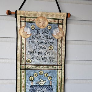 May include: Woven wall hanging with a wooden dowel and black cord. The tapestry features a central panel with the text "I will sleep in peace, for you alone O LORD make me dwell in safety." The design includes moons, stars, and a dove.
