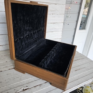 May include: A wooden silverware box with a black velvet interior and slots for holding silverware. The box is open and the lid is propped up.