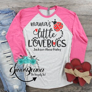 Pode incluir: Uma camisa de manga comprida branca e rosa com um design de camisa de beisebol. A camisa tem o texto "mama's little lovebugs" com um gráfico de joaninha e os nomes "Jackson-Alexa-Hailey" impressos nela.