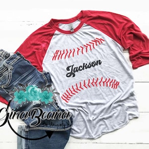 May include: White and red baseball raglan t-shirt with a baseball graphic and the name "Jackson" in a retro font.