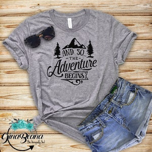 May include: Gray t-shirt with a black graphic that says "And so... the adventure begins" with a mountain and pine trees.