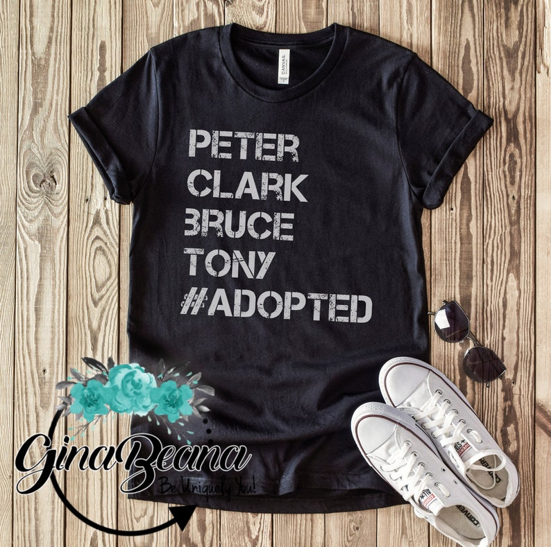 May include: Black t-shirt with white text that reads "Peter Clark Bruce Tony #Adopted".