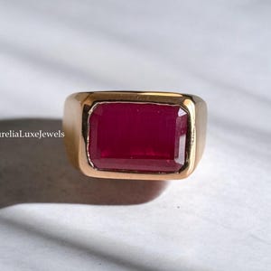 May include: A gold ring with a large, rectangular, red ruby gemstone.
