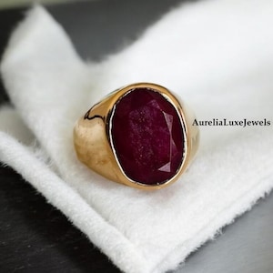 May include: A gold ring with a large, oval-shaped ruby gemstone. The ring has a simple, classic design.