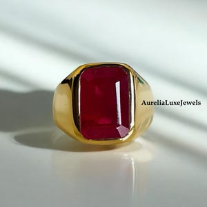 May include: A gold ring featuring a large, rectangular, red gemstone. The ring is set in a simple, classic style.