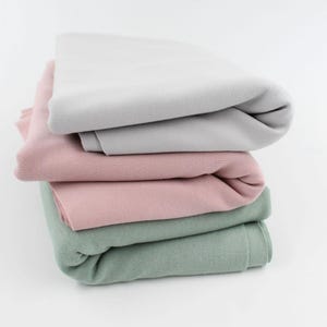 Könnte beinhalten: Ein Stapel von vier Stoffproben in verschiedenen Farben: hellgrau, rosa, grün und dunkelgrün. Der Stoff ist gefaltet und die Kanten sind sichtbar.