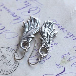 May include: A pair of silver earrings with a delicate, leafy design. The earrings are dangle style and have a simple hook closure.