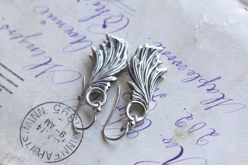 May include: A pair of silver earrings with a delicate, leafy design. The earrings are dangle style and have a simple hook closure.