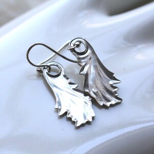 May include: A pair of silver earrings with a leaf design. The earrings are made of a smooth, shiny metal and have a delicate, feminine look.