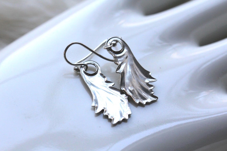 May include: A pair of silver earrings with a leaf design. The earrings are made of a smooth, shiny metal and have a delicate, feminine look.