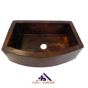 May include: A large, copper farmhouse sink with a hammered finish. The sink is curved at the front and has a single drain hole.
