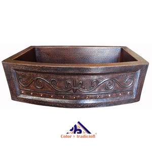 May include: A copper farmhouse sink with a hammered finish and an ornate design around the top edge. The sink is curved at the front.