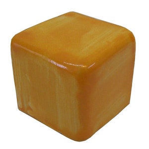 May include: A square, amber-colored decorative object with rounded corners. The object has a glossy finish and a marbled appearance, with lighter streaks running through the amber color. The object is a cube shape.