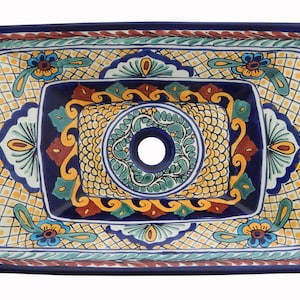 May include: Rectangular ceramic sink with a vibrant, hand-painted design. The sink features a deep blue border and a central drain hole. The intricate pattern includes yellow, blue, green, and red floral and geometric motifs, creating a decorative and artistic piece.