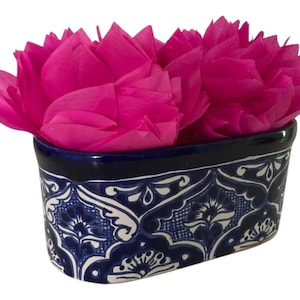 May include: A rectangular ceramic container with a dark blue rim and intricate white and blue floral patterns. The container is filled with bright pink tissue paper, creating a vibrant contrast. This decorative piece is ideal for holding small items or as a decorative accent.