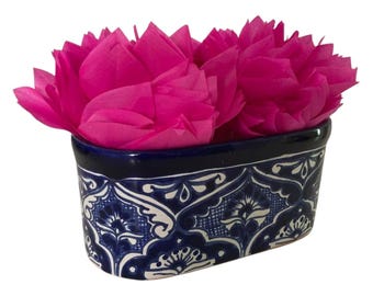 May include: A rectangular ceramic container with a dark blue rim and intricate white and blue floral patterns. The container is filled with bright pink tissue paper, creating a vibrant contrast. This decorative piece is ideal for holding small items or as a decorative accent.