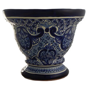 May include: A large, blue and white ceramic planter with intricate floral designs. The planter has a wide, round opening and a flared base.