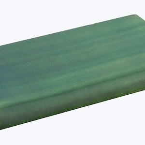 May include: A green ceramic tile with a slightly rounded edge. The tile has a subtle, textured finish.