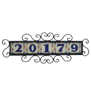 May include: A black metal frame with a scrolled design holds a row of five white ceramic tiles with blue numbers, "20179", and colorful floral patterns.