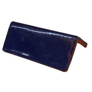 May include: A navy blue ceramic tile corner piece with a glossy finish. The L-shaped tile has a smooth, reflective surface and a visible brown edge. This tile is suitable for various home improvement projects.