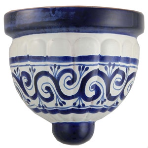 May include: A white ceramic wall planter with a blue and white swirl design. The planter has a rounded shape with a small lip at the top and a rounded base.