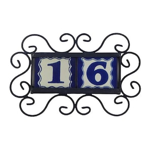May include: A blue and white ceramic house number sign with the number 16 on it. The sign is framed in black metal with a decorative scroll design.