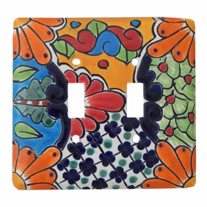 May include: A decorative ceramic double light switch cover with a vibrant floral design. The cover features orange, red, blue, and green flowers and foliage against a yellow and white background. The design is hand-painted with intricate details.