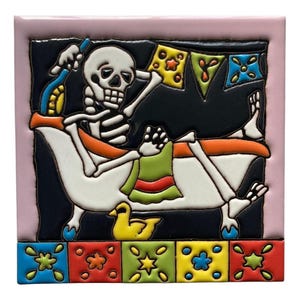 May include: A decorative ceramic tile featuring a skeleton relaxing in a bathtub. The skeleton is holding a bottle and towel, with colorful bunting overhead. The tile has a pink border and a row of colorful square tiles at the bottom.