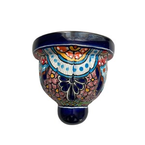 May include: A hand-painted ceramic wall pocket with a vibrant floral design. The piece features a deep blue rim and base, with a colorful pattern of flowers and geometric shapes in shades of orange, pink, and turquoise. The wall pocket is designed to be mounted on a wall.