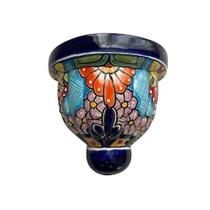 May include: A hand-painted ceramic wall pocket with a vibrant floral design. The piece features a deep blue rim and base, with a colorful array of orange, purple, and blue flowers. This decorative item is perfect for adding a touch of artistry to any space.