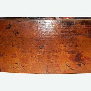 May include: A large, copper farmhouse sink with a hammered finish. The sink is oval shaped and has a rustic, aged look.