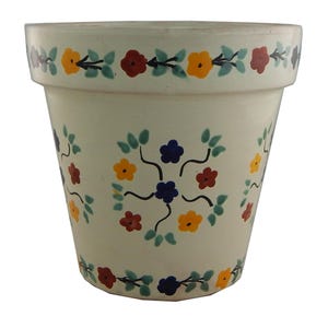 May include: Cream-colored ceramic flower pot with a floral design. The pot features a repeating pattern of yellow, red, and blue flowers with green leaves. The rim of the pot has a similar floral border.