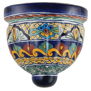 May include: A hand-painted, ceramic wall planter with a vibrant, floral design. The planter features a deep blue base with colorful accents of yellow, green, and red. The rim has a decorative border, and the overall shape is rounded with a small, rounded base.