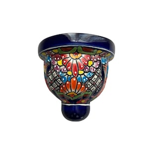 May include: A hand-painted, ceramic wall pocket with a vibrant floral design. The piece features a deep blue rim and base, with a colorful array of flowers in red, orange, yellow, and blue. The wall pocket is a decorative item.