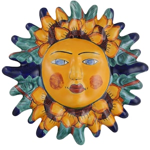 May include: A ceramic sun wall hanging with a yellow face, blue eyes, and red lips. The sun is surrounded by a sunflower design with yellow petals and green leaves. The background is blue.