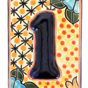 May include: A ceramic tile with a colorful Mexican-style design featuring a blue number "1" in the center. The tile has a yellow background with orange and black geometric patterns and blue and green floral accents.